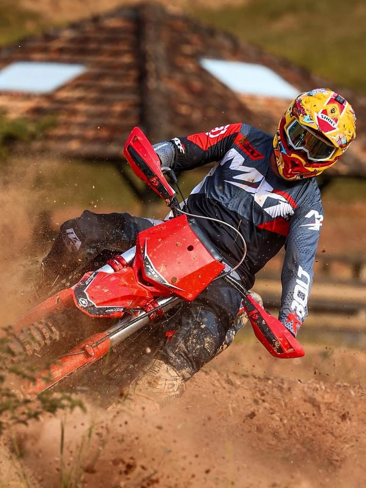 Piloto fazendo curva na terra com uma moto MXF vermelha
