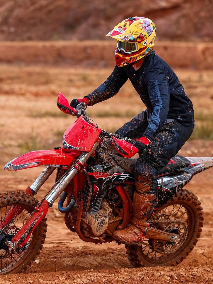 Piloto de capacete amarelo pilotando uma moto MXF na terra